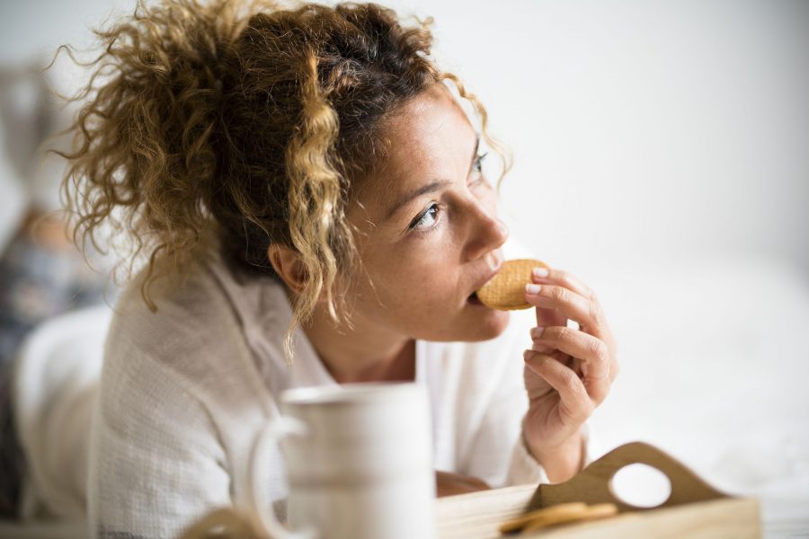 Portrait Of Adult Beautiful Woman Eating Cookie In Morning Breakfast In The Bedroom - Home Or Hotel
